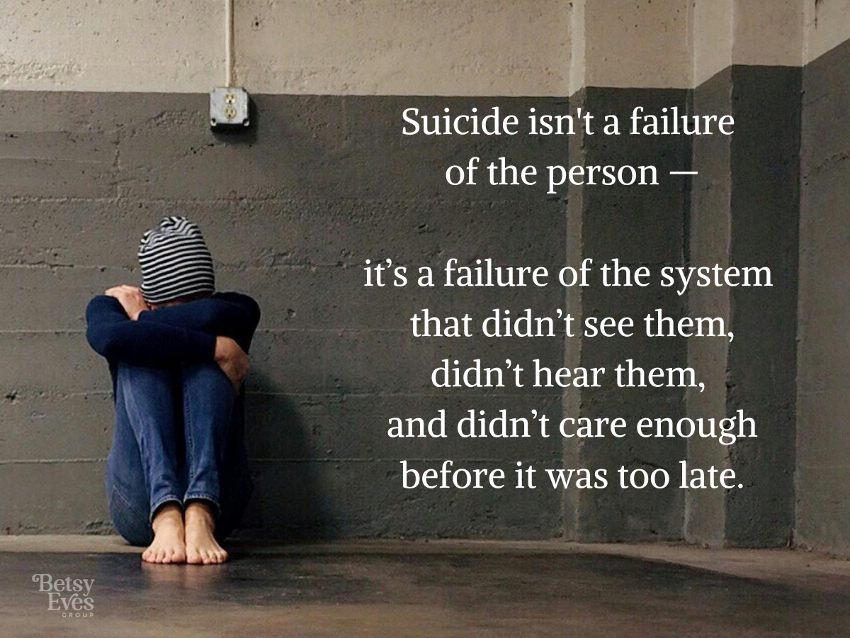 Image of a person sitting on the ground with their knees tucked to their chest and head down.   With text overlay that says: Suicide isn't a failure of the person - it's a failure of the system that didn't see them, didn't hear them, and didn't care enough before it was too late.